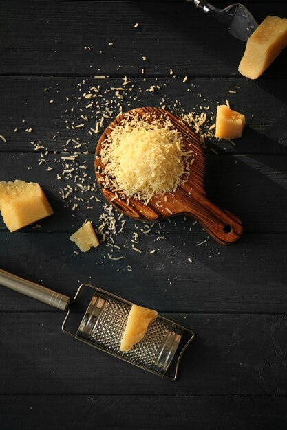 Wooden board with cheese and grater on table