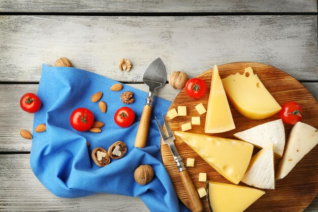 Wooden board with cheese tomatoes and nuts on blue napkin