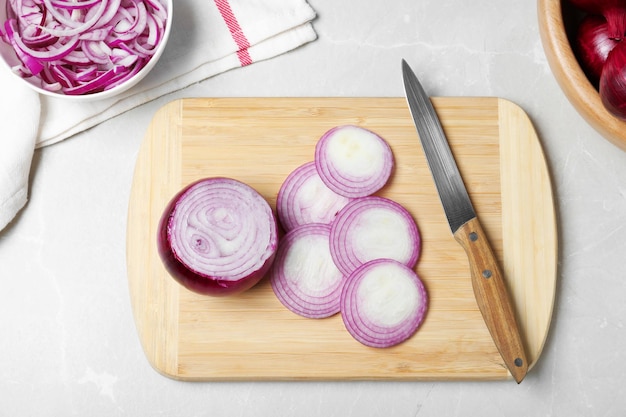 Photo wooden board with cut fresh red onion and knife on marble table flat lay