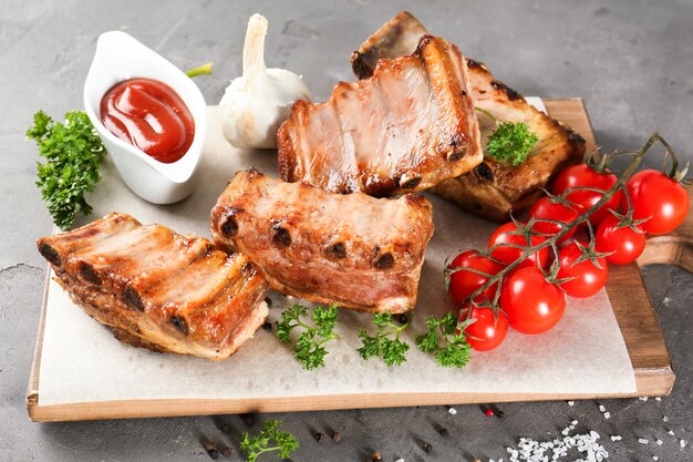 Wooden board with delicious grilled ribs tomatoes and sauce on table