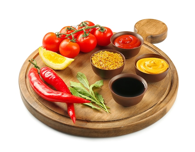 Wooden board with different sauces and vegetables on white surface