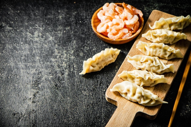 A wooden board with dumplings and a bowl of shrimp.