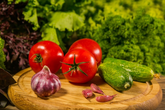 Una tavola di legno con pomodori freschi, aglio e cetrioli.