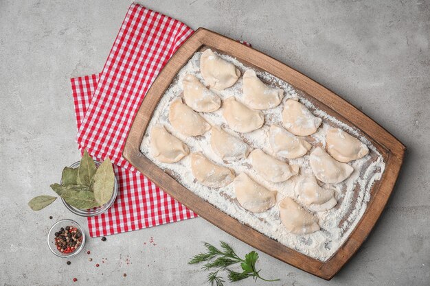 Wooden board with raw dumplings on table top view