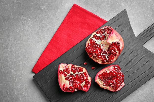 Wooden board with ripe pomegranate on grey background