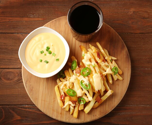 Wooden board with tasty cheese fries sauce and glass of soda water on table