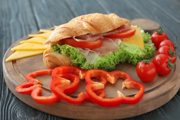 Wooden board with tasty croissant sandwich on table