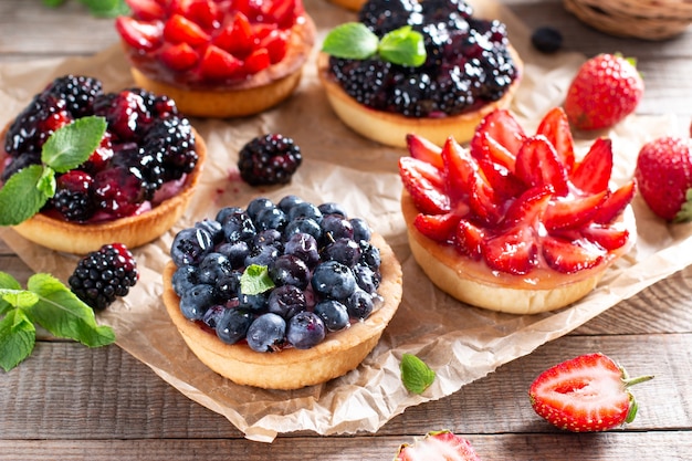 Wooden board with tasty tartlets on table. Summer dessert, healthy morning breakfast or snack, open sandwiches with strawberry, blueberries, blackberries.