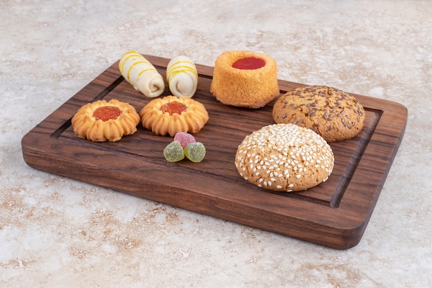 A wooden board with various types of sweet cookies on a stone surface.