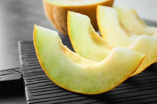 Photo wooden board with yummy melon slices on table