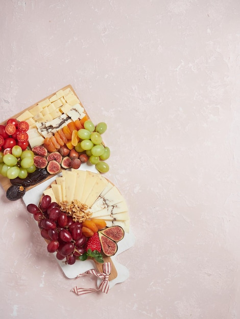 Tavole di legno con formaggi e frutta assortita su sfondo rosa vista dall'alto con spazio negativo