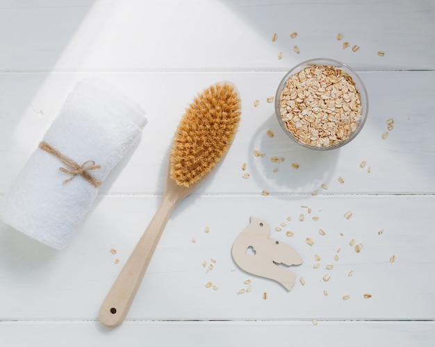 Spazzola per il corpo in legno, asciugamano bianco e farina d'avena cruda su un fondo di legno bianco