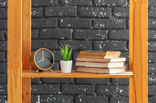 Photo wooden bookshelf with books and stuff against black brick wall