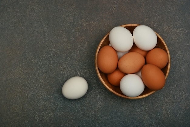 Ciotola di legno di uova di gallina marrone sul tavolo scuro