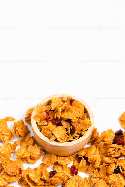 The wooden bowl of caramel cornflakes with raisins on white background for healthy eating and breakfast concept