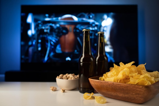 백그라운드에서 칩과 스낵의 나무 그릇 TV 작동 맥주 한 잔과 함께 집에서 영화 또는 TV 시리즈를 보는 아늑한 저녁