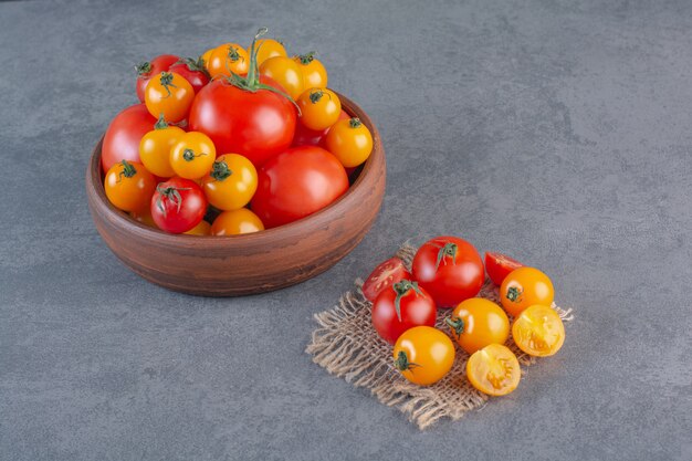 Wooden bowl of colorful organic tomatoes on stone background.