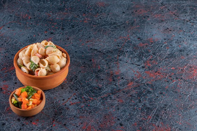 Wooden bowl of delicious seashell pasta and mini salad on marble surface. 