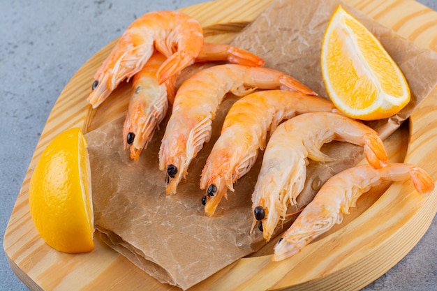 A wooden bowl of delicious shrimps with sliced lemon on a stone surface 