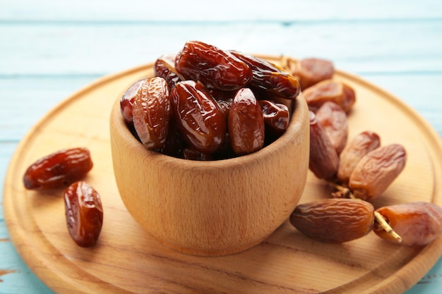 Wooden bowl of dried dates on blue wooden background. Branch with dates on grey.