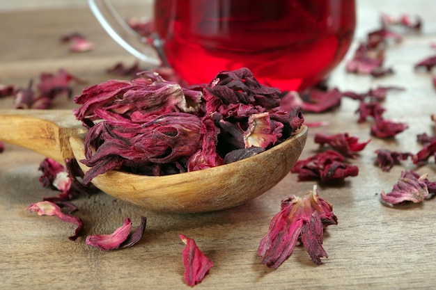 a wooden bowl of dried pink flowers with a glass of red tea.