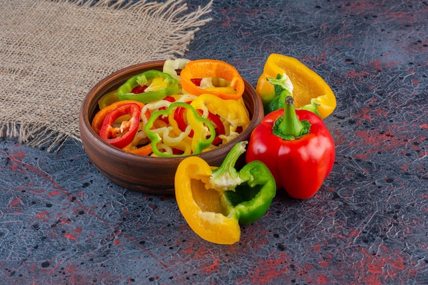 Wooden bowl full of chopped colorful peppers on marble surface