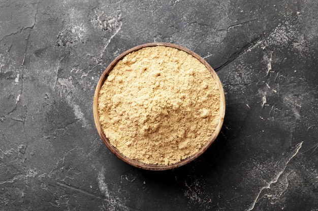 Wooden bowl full of dry ginger on textured background