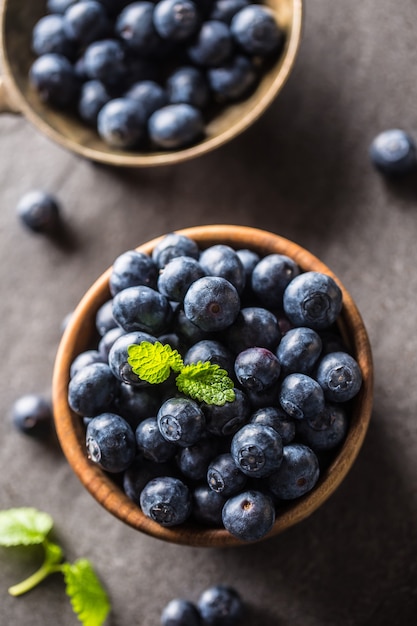 Wooden bowl full of fresh blueberries with herbs.