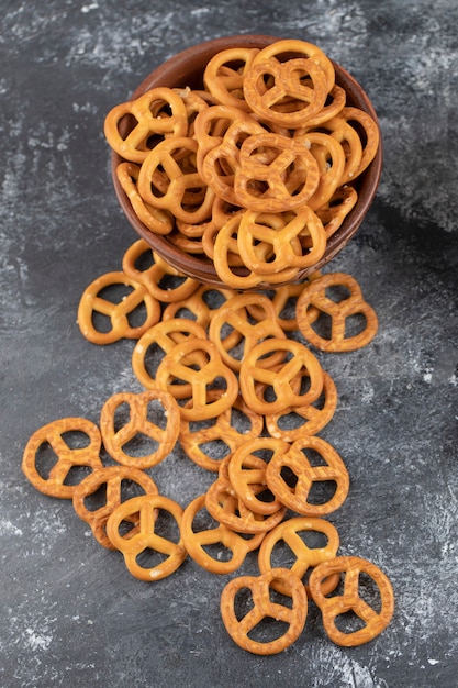 Photo wooden bowl full of salted dry pretzels on white surface.