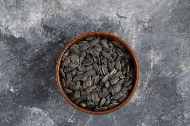 Photo wooden bowl full of sunflower black seeds placed on white surface