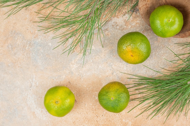 Wooden bowl of green fresh tangerines on marble surface.