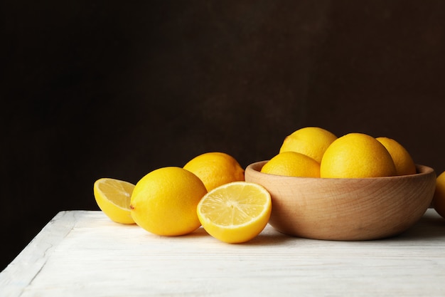 Wooden bowl and lemons against brown surface