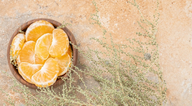 A wooden bowl of peeled tangerine on a stone surface