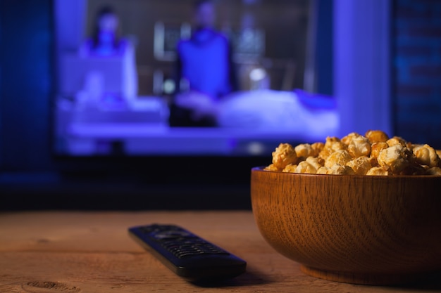 A wooden bowl of popcorn and remote control.