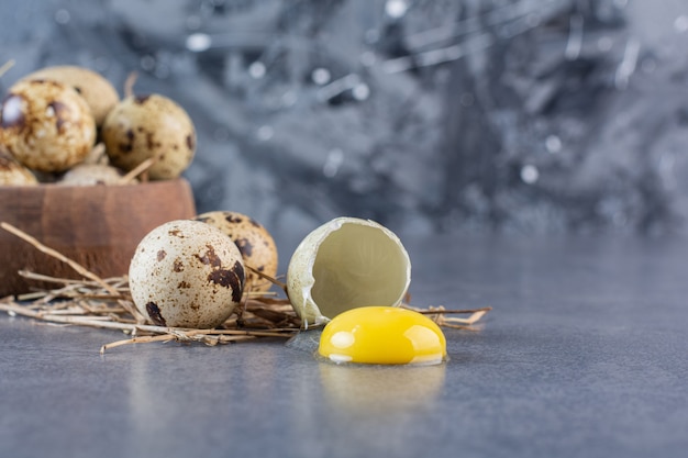 Wooden bowl of raw quail eggs on stone table.