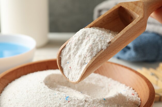 Wooden bowl and scoop with laundry powder, close up