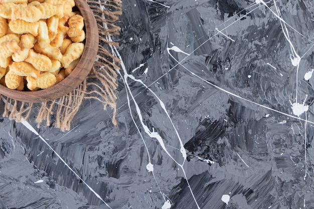 Wooden bowl of tasty salted crackers on marble background.