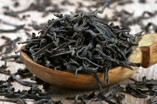 A wooden bowl of tea is filled with tea leaves.