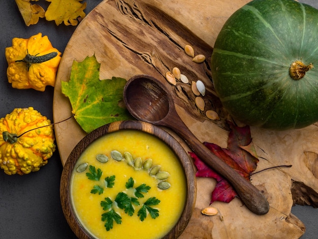 Wooden bowl of traditional pumpkin soup on gray table decorated with seeds parsley colorful foliage decorative pumpkin