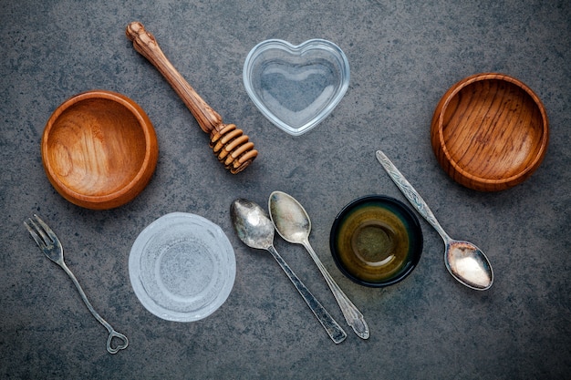 Wooden bowl and vintage spoons and honey dipper on dark stone background with flat lay .