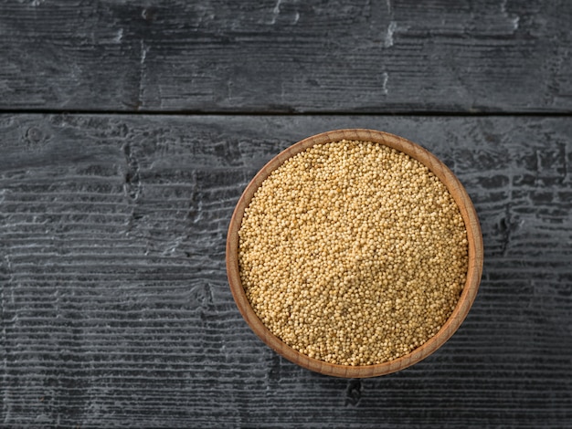 Wooden bowl with amaranth seeds on dark wooden table