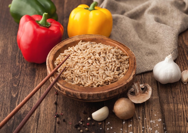 Wooden bowl with boiled long grain risotto rice with mushrooms on wooden background with sticks and linen kitchen towel and paprika pepper with garlic