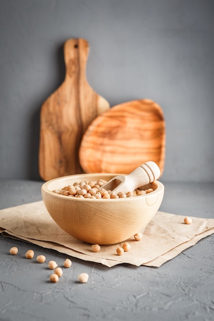 Wooden bowl with dry raw organic chickpeas on gray concrete background