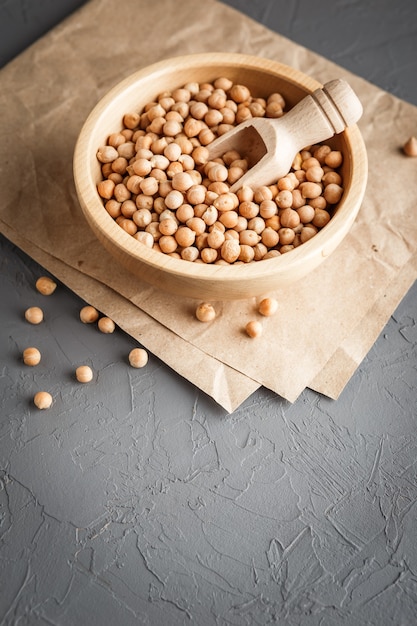 Wooden bowl with dry raw organic chickpeas on gray concrete background