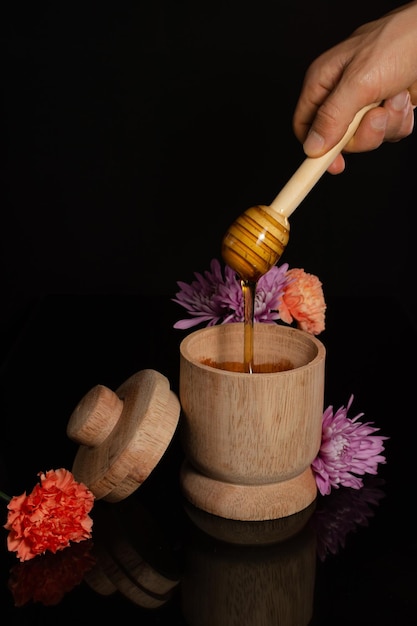 Wooden bowl with honey dipper dripping honey with flowers isolated in black background