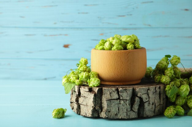 Wooden bowl with hops on blue wooden background, space for text. Top view