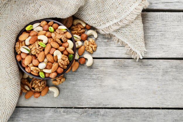 Photo wooden bowl with nuts on a wooden background, near a bag from burlap.