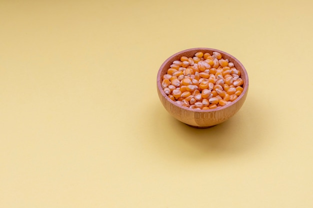 Wooden bowl with popcorn corn, yellow background.