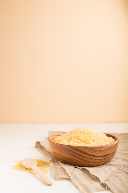 Wooden bowl with raw golden rice on a white wooden background