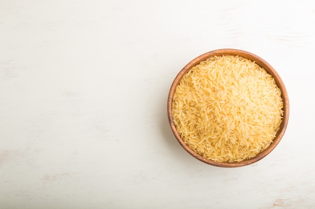 Wooden bowl with raw golden rice on a white wooden